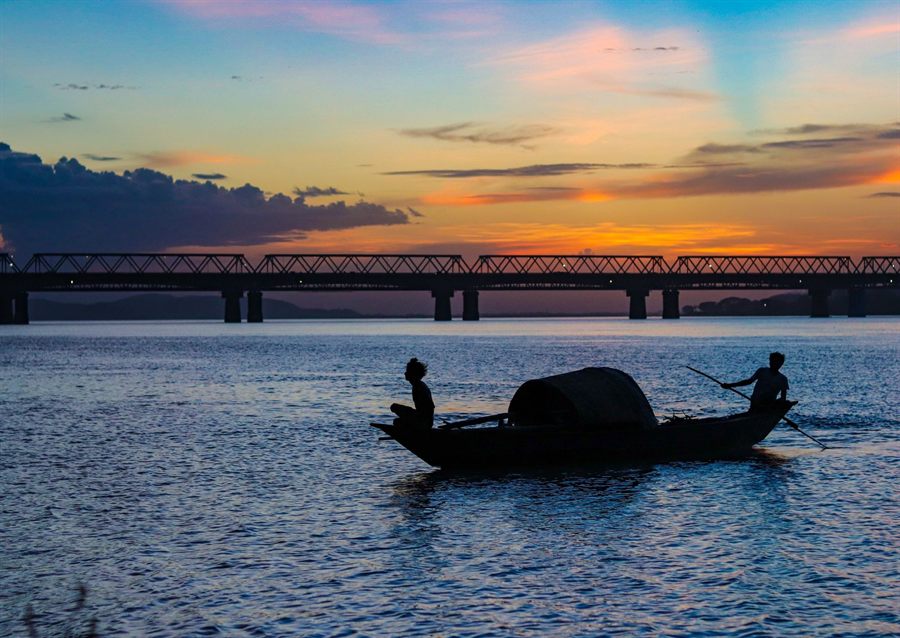 Silhouetted boatmen on the Brahmaputra at sunset with a long bridge behind